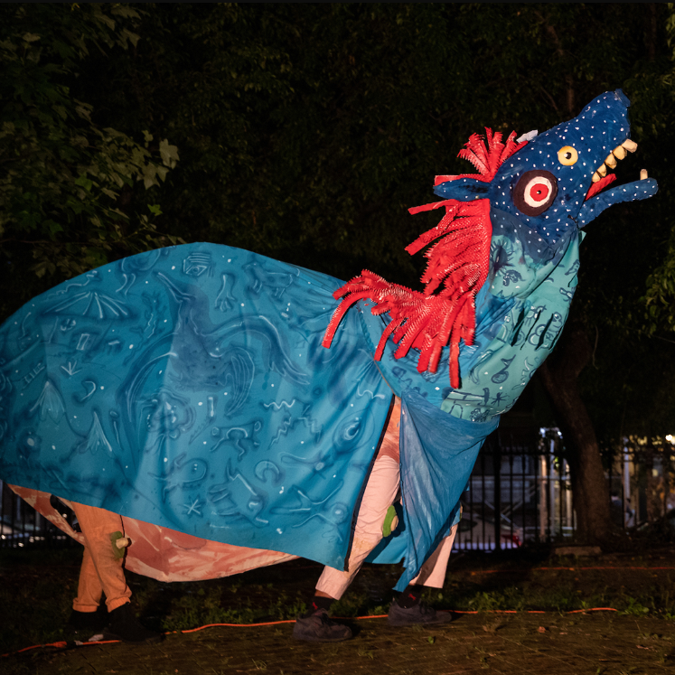 A horse-like puppet made of foam, with two sets of human legs, wanders through a park at night.